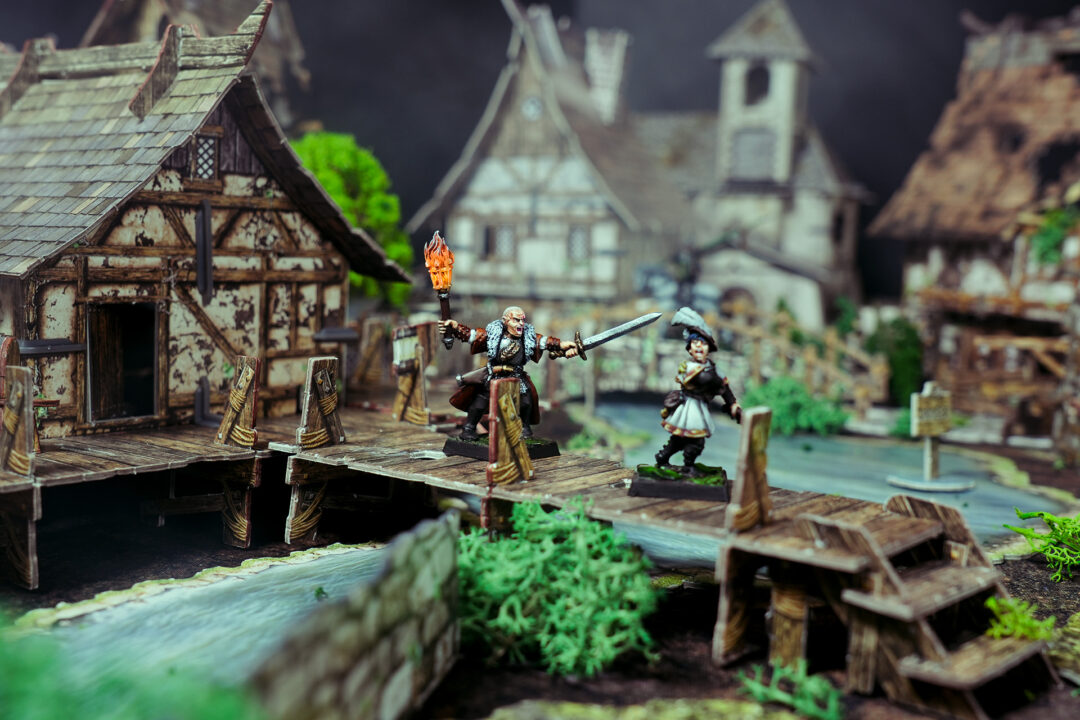 A witch hunter directs other members of his warband to cross a bridge.