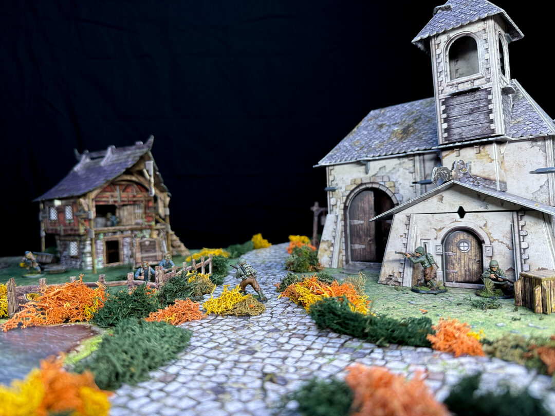 Bolt Action German and American troops fight on a battlefield using the Battle Systems Fantasy Chapel and Barn