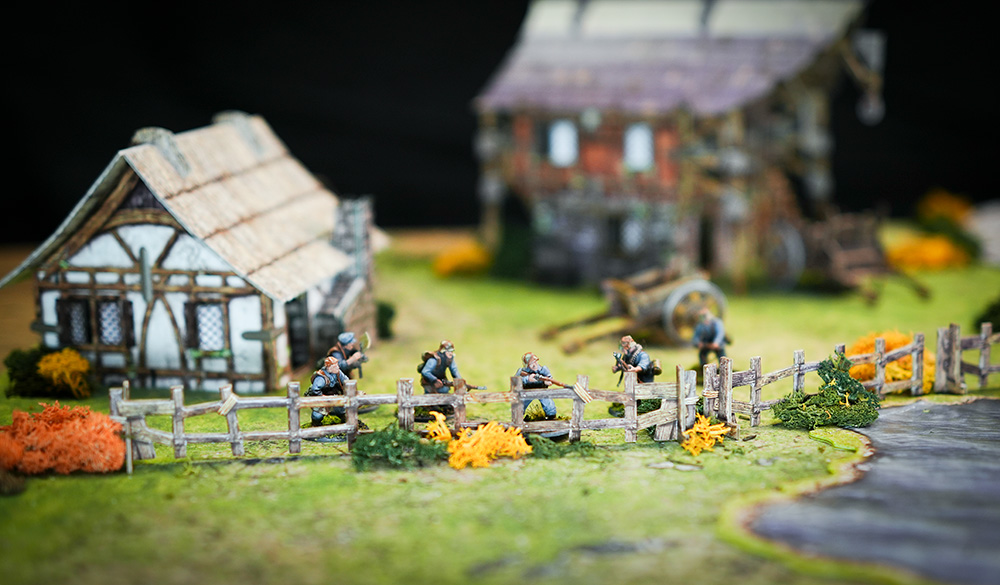 Bolt Action German troops take cover on a fenceline using Battle Systems terrain. The fantasy Barn and cottage sets are used.