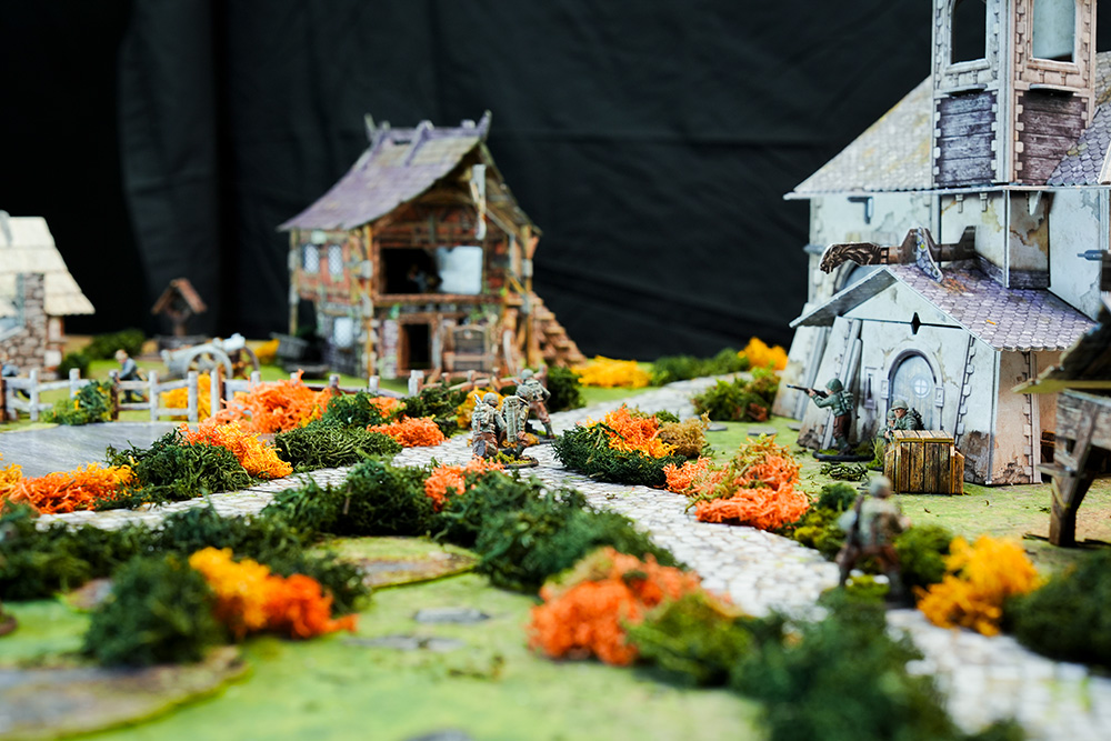 Bolt Action German and American troops fight on a battlefield using the Battle Systems Fantasy Chapel and Barn